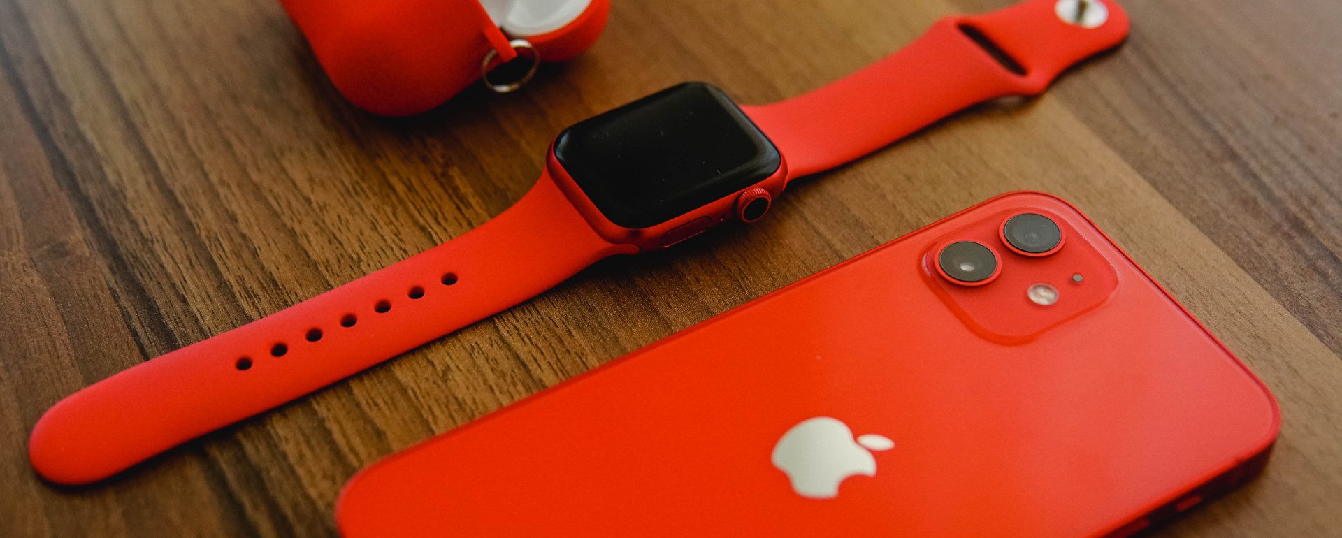 red apple watch, iphone and earpods case on smooth wooden table