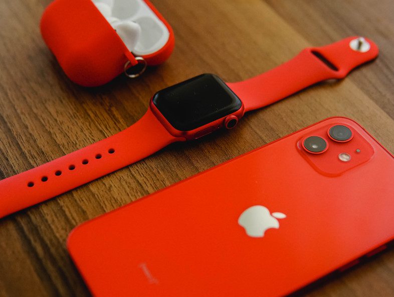 red apple watch, earpods and iphone on a smooth wooden table